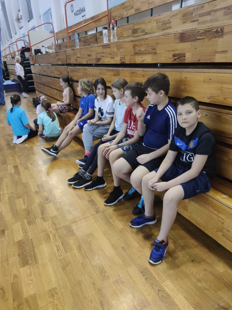 Uczniowie siedzący na trybunach hali sportowej